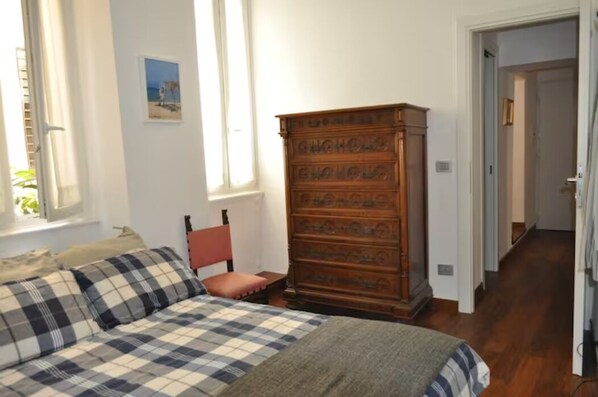 Une chambre à coucher avec un lit, une commode en bois, une chaise et une fenêtre.