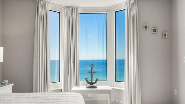 Una camera da letto con un letto grande, un tavolino con decorazione a forma di ancora e vista sull'oceano attraverso una finestra a bovindo.
