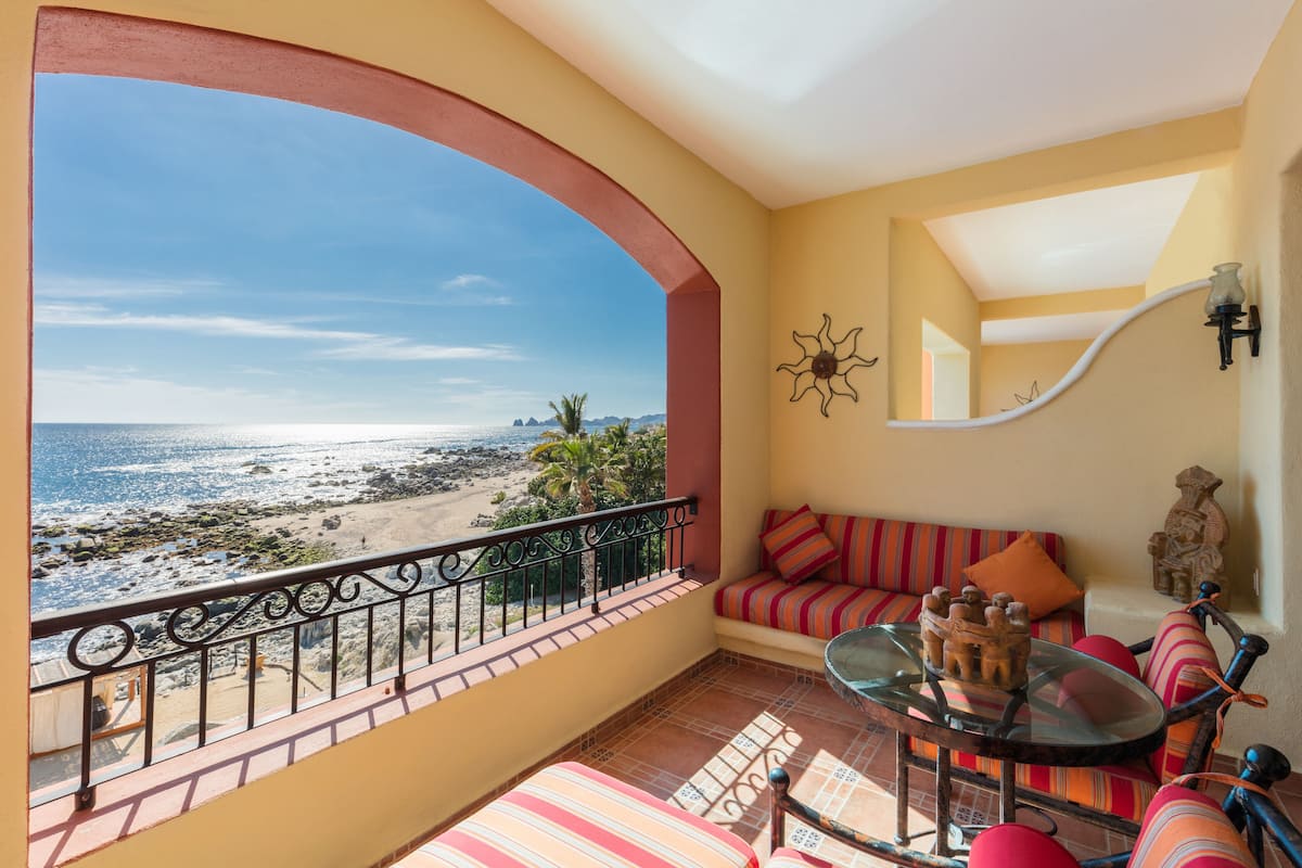 Un balcón con vista a la playa, una mesa de vidrio, un sofá con cojines a rayas y un adorno en la pared.