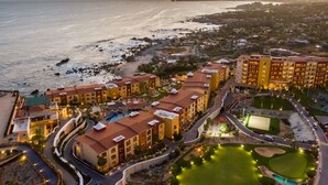 Vue aérienne d’un complexe hôtelier comprenant plusieurs bâtiments, une plage et un parcours de golf.