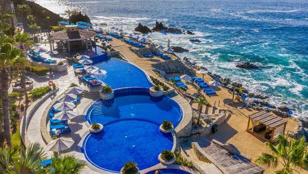 Un complexe hôtelier doté d’une grande piscine, de chaises longues situées au bord de la plage et offrant une vue sur l’océan.