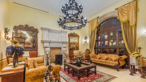 Un salon spacieux avec un grand canapé, une cheminée, un lustre et une grande fenêtre agrémentée de rideaux.