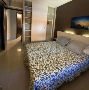 Ein modernes Schlafzimmer mit einem gemusterten Bettbezug, einem eingebauten Kleiderschrank und einem Bild an der Wand.