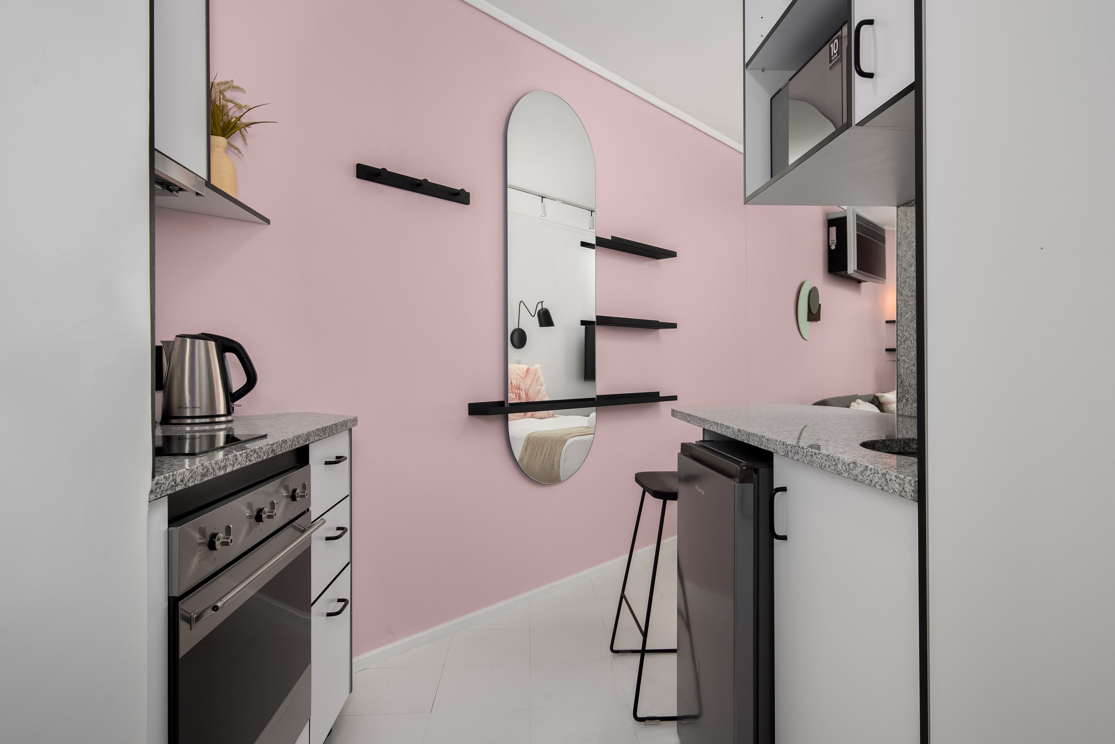 A modern kitchen with a pink wall, a large mirror, and a countertop with a kettle.