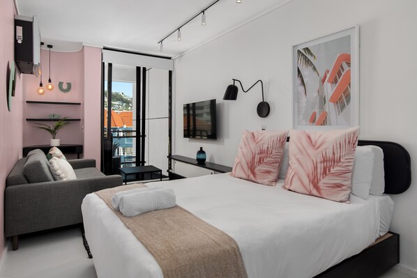 A modern bedroom with a bed, a sofa, a desk, and a TV. - The Flamingo 408 (Cape Town)