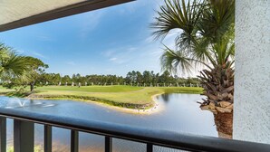 A view of a golf course with a water body, palm trees, and a clear sky. - Edgewater Villa #1913 | Beach Access, Pools, & Golf! (Panama City Beach)