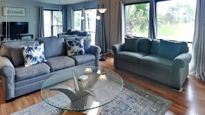 A living room with two sofas, a glass coffee table, and a TV in the background. - Edgewater Villa #1913 | Beach Access, Pools, & Golf! (Panama City Beach)