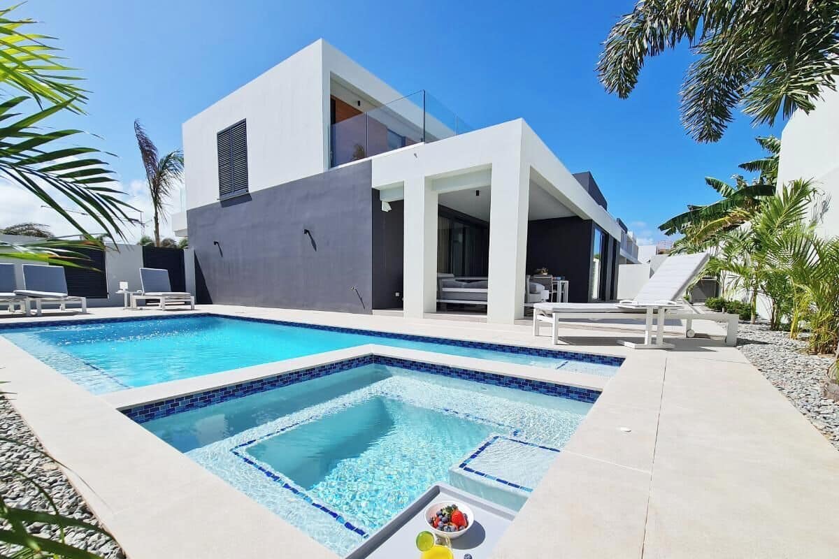 Un área de piscina moderna con una piscina rectangular, sillas de descanso y un edificio contemporáneo al fondo.