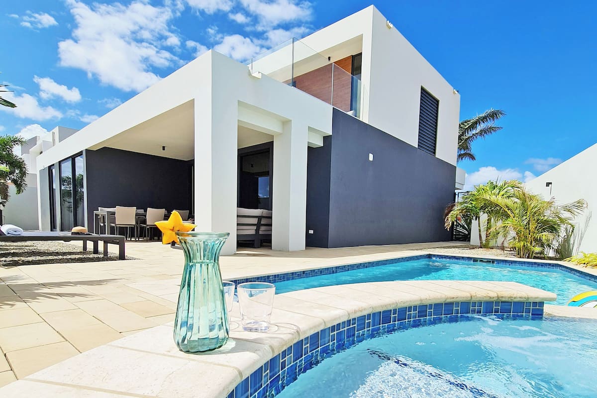 Un área moderna junto a la piscina con una piscina azul cristalina, un florero de vidrio y una zona de comedor.