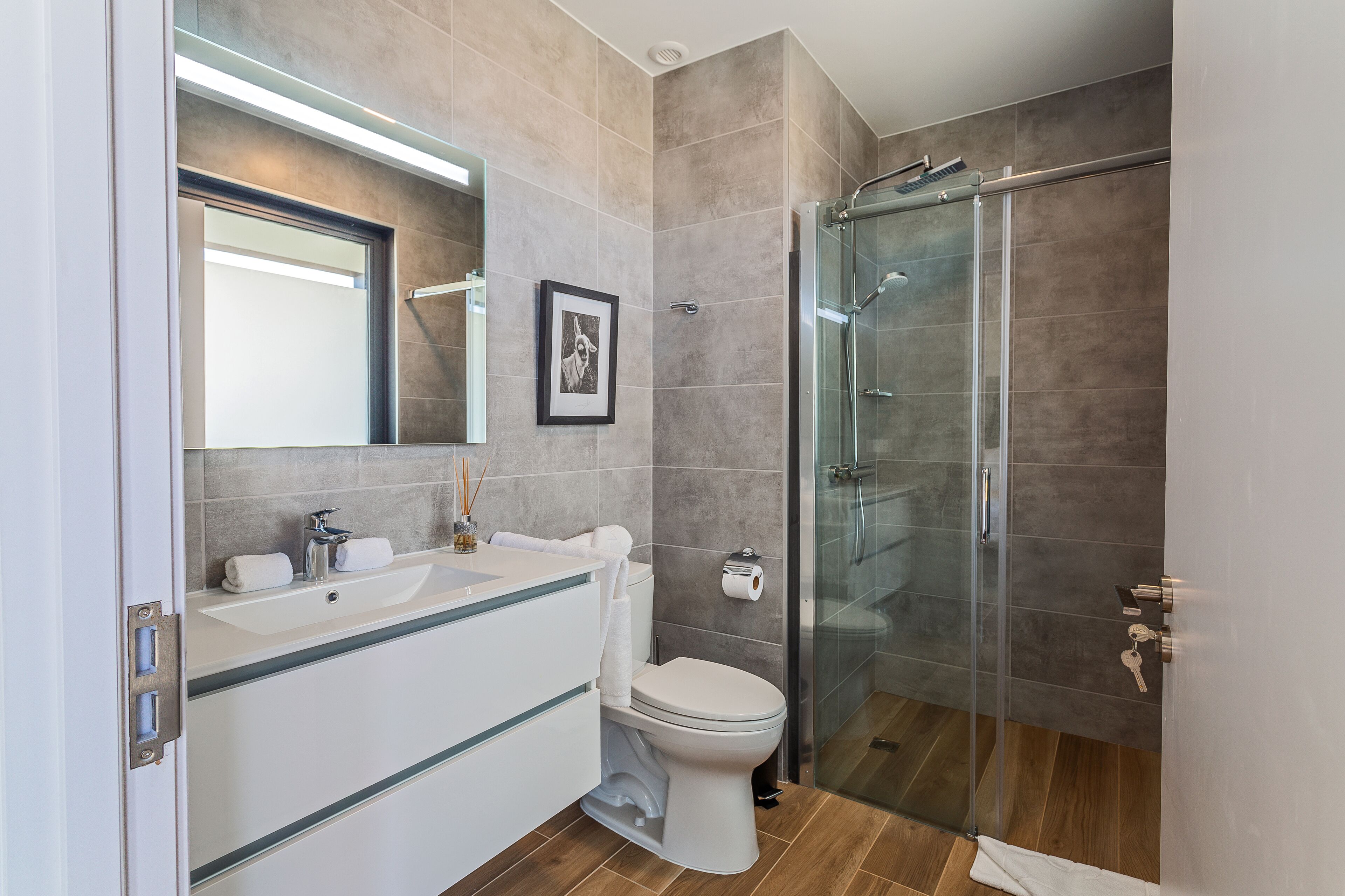 Un bany modern amb una cabina de dutxa de vidre, un rentapeus blanc i un vàter.