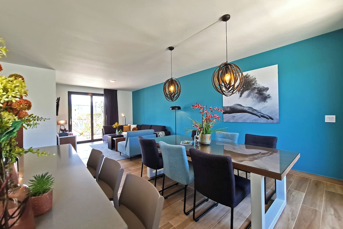 Un área de comedor moderna con una mesa de vidrio, sillas tapizadas en azul y un cuadro grande en la pared.