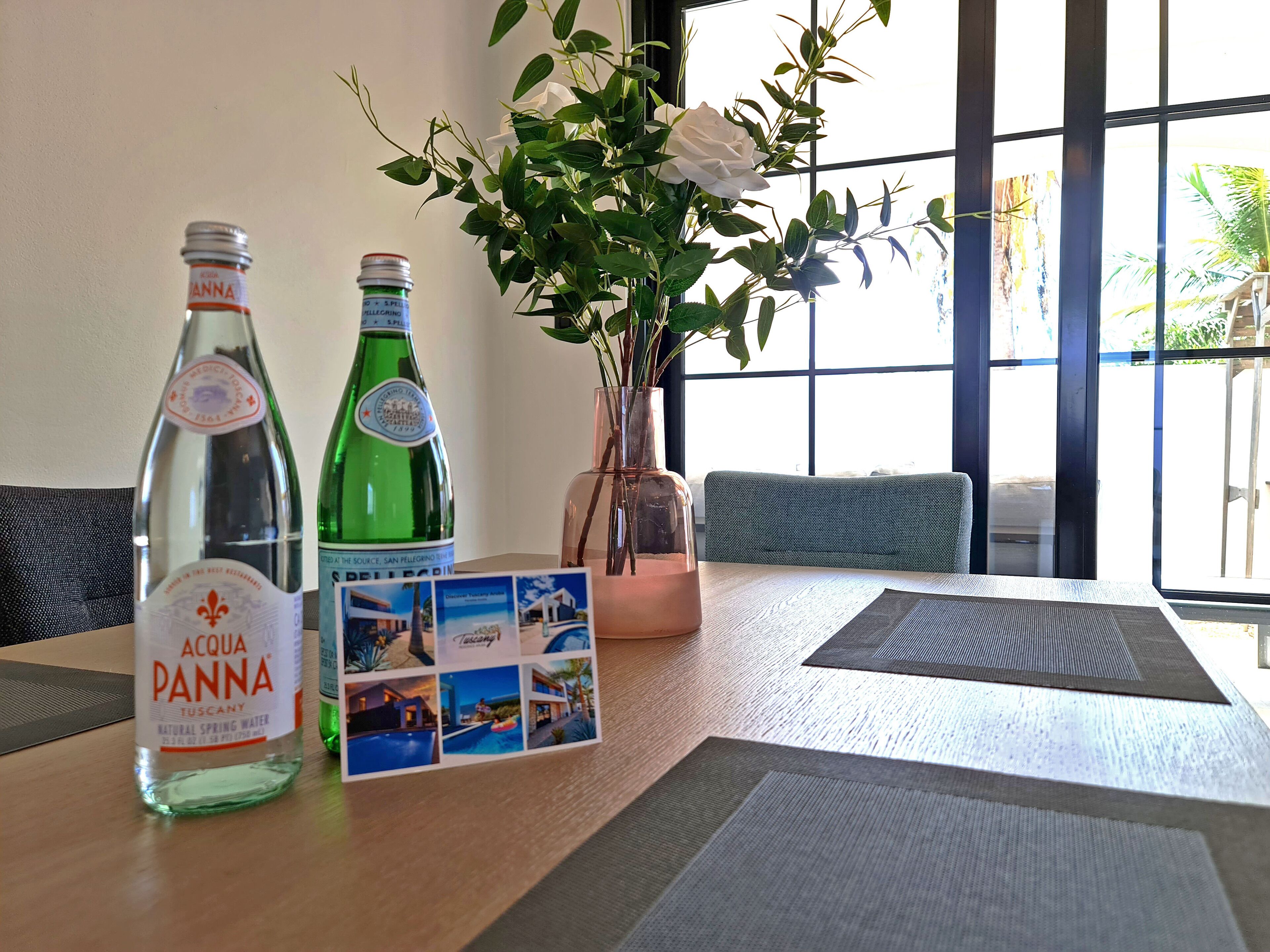 A table with two bottles of Acqua Panna water, a brochure, and a vase with a white rose.