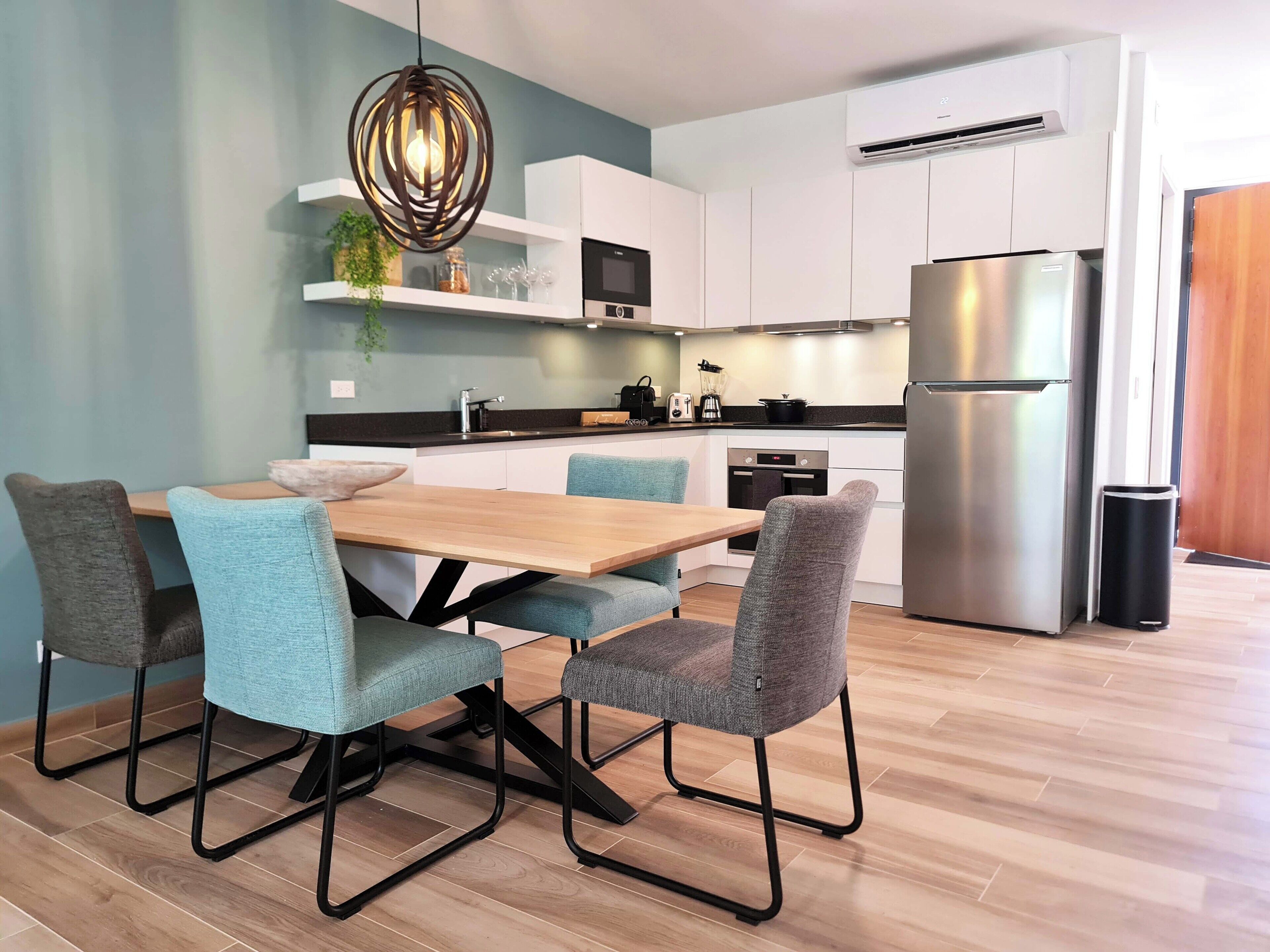 Une cuisine moderne avec des meubles blancs, un réfrigérateur en acier inoxydable et une table à manger en bois, accompagnée de quatre chaises.