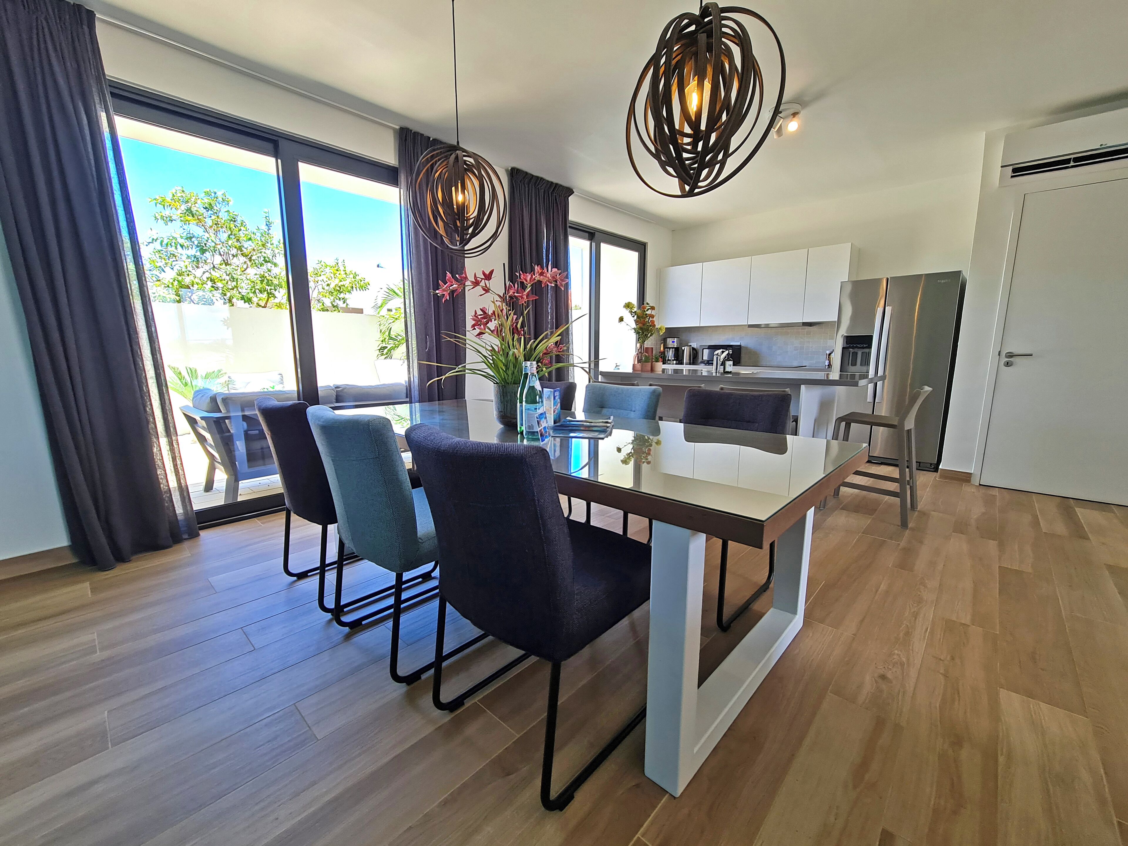 A modern kitchen with a central island, dining area with chairs, and a large window with curtains.