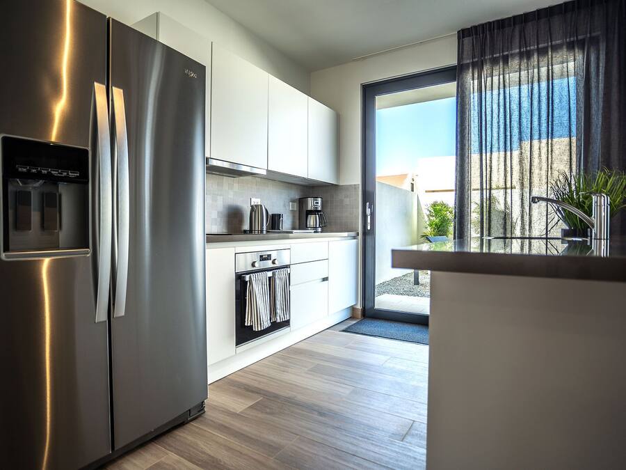 Una cocina moderna con electrodomésticos de acero inoxidable, una cafetera y vistas al exterior a través de un ventanal corredero.