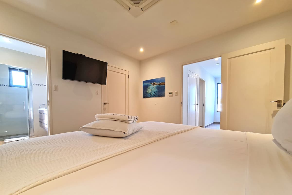 Un dormitorio con una cama grande, un televisor de pantalla plana en la pared y un cuadro sobre la cama.