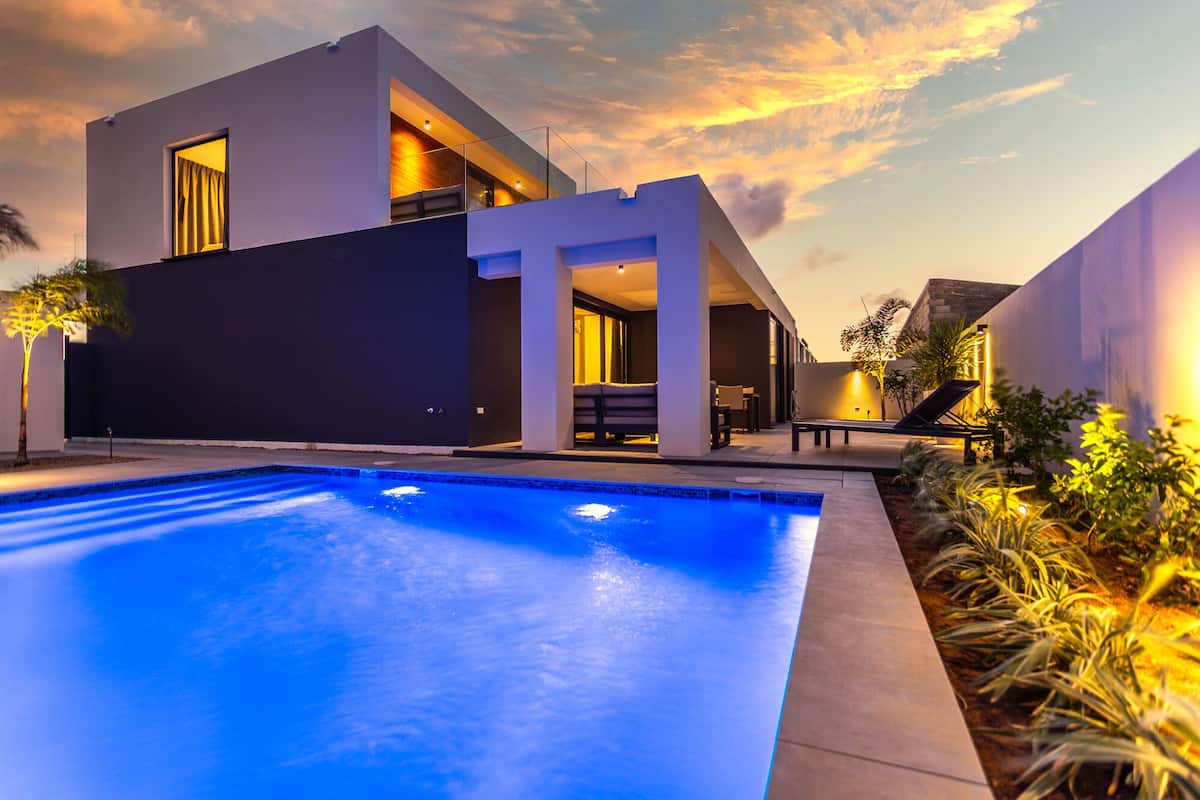 Un área moderna junto a la piscina con una piscina cristalina, un espacio de descanso cubierto y un edificio con amplios ventanales.