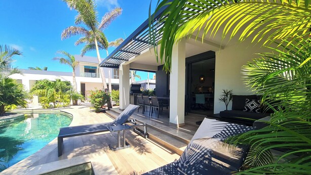 Un área de piscina moderna al aire libre con sillones de descanso, una parrilla y un comedor.