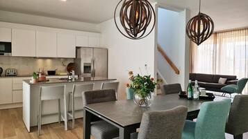 Una cocina moderna con armarios blancos, un refrigerador de acero inoxidable y una zona de comedor con mesa y sillas.