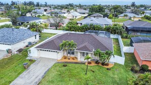 A residential house with a large garage, surrounded by a well-maintained lawn and palm trees. - AMAZING HOUSE NEAR THE BEACHES OF SOUTH FLORIDA (Cape Coral)