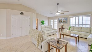 A spacious living room with a beige color scheme, featuring a large white sofa, a smaller sofa, a coffee table, and a ceiling fan. - AMAZING HOUSE NEAR THE BEACHES OF SOUTH FLORIDA (Cape Coral)