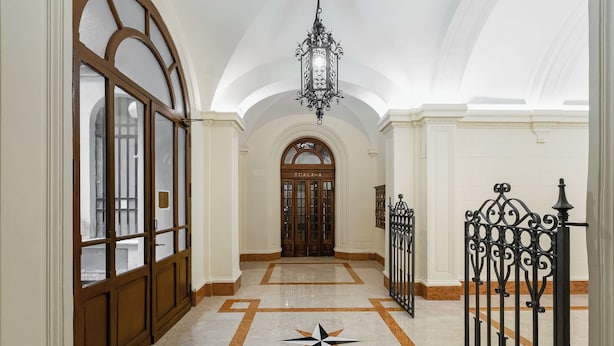 Un pasillo con piso de mármol, un diseño de estrellas, una reja de hierro forjado y una puerta con la etiqueta 'SCALA A'.