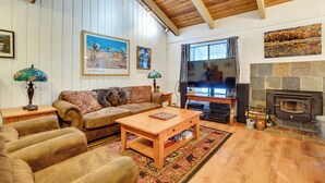 A cozy living room with a wooden ceiling, a fireplace, a sofa, a coffee table, and a television. - Mammoth Lakes Condo ~ 5 Mi to Mammoth Mtn! (Mammoth Lakes)