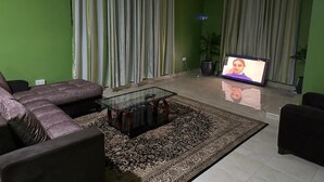 Ein Wohnzimmer mit Ecksofa, Glastisch, gemustertem Teppich und Flachbildfernseher.