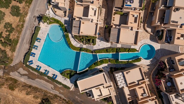 An aerial view of a residential area with a large swimming pool, multiple houses, and a road. - PP 6/40, a bedroom apt in a complex with communal pools at Plakias (Plakias)