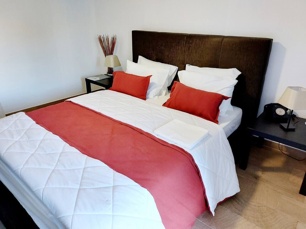 A bed with a quilted white and red bedspread, a dark headboard, and a nightstand with a lamp and a radio.