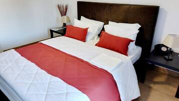 A bed with a quilted white and red bedspread, a dark headboard, and a nightstand with a lamp and a radio.