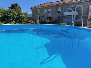 A clear blue swimming pool with a ladder, surrounded by a stone building with a tiled roof.