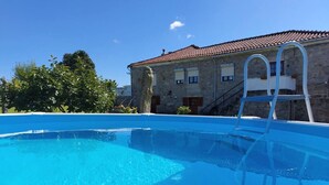 A clear blue swimming pool with a ladder, a stone building with a tiled roof, and trees in the background. - Rural farm - Queen room with breakfast (Viana do Castelo)