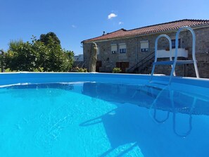 A clear blue swimming pool with a ladder, a stone building with a tiled roof, and trees in the background. - Rural farm - Queen room with breakfast (Viana do Castelo)