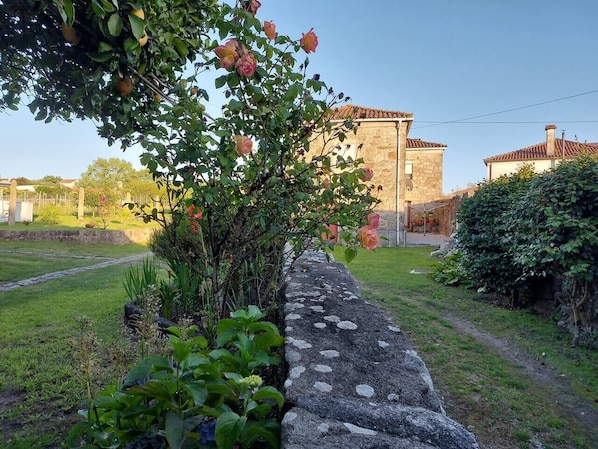 A stone wall with a garden path, a stone building, and a clear sky.