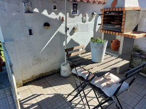 An outdoor seating area with a table and chairs, a potted plant, a barbecue grill, and a tiled floor. - Rural farm - Queen room with breakfast (Viana do Castelo)