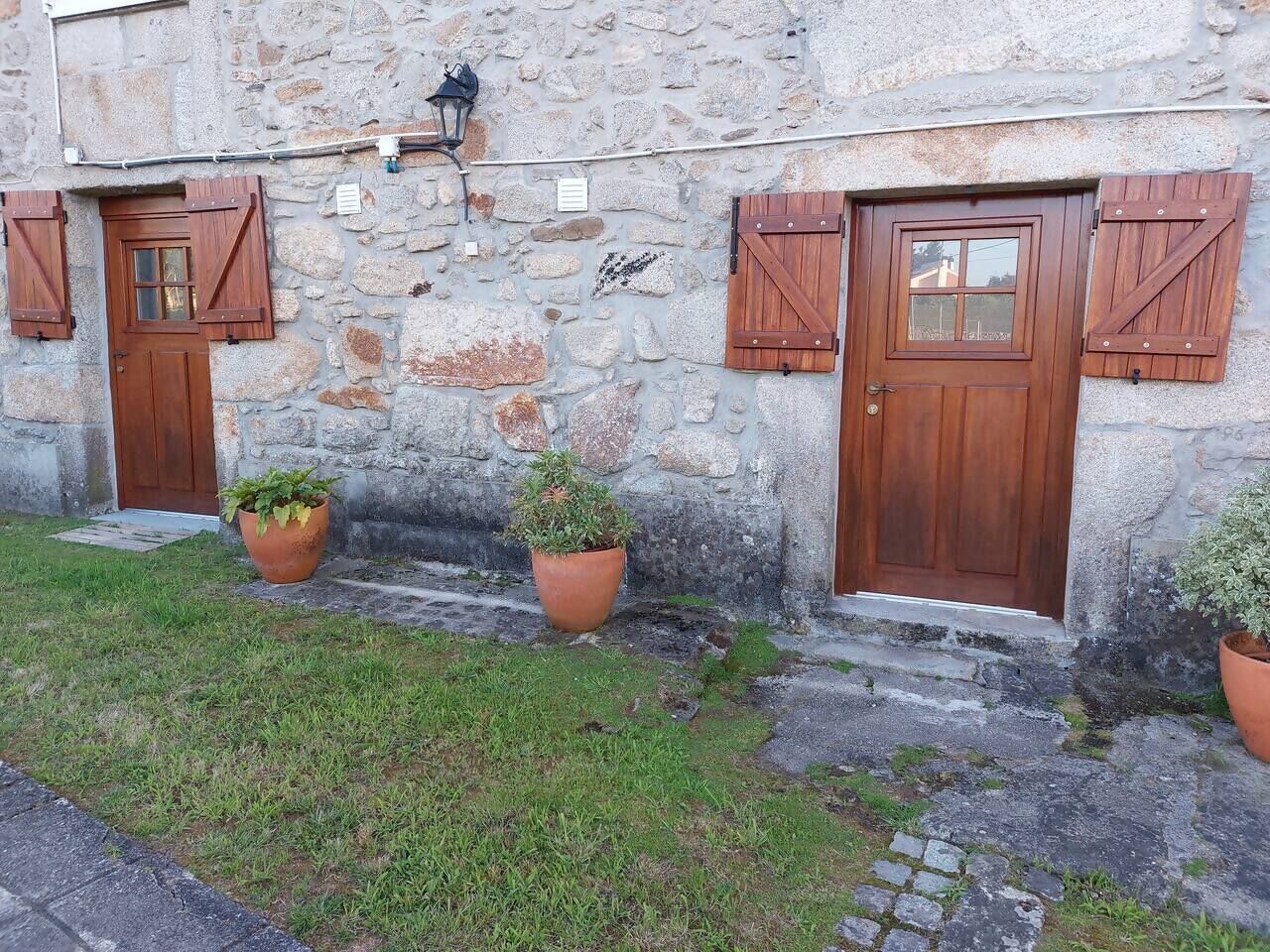 Un bâtiment en pierre doté de deux portes en bois, chacune avec des volets, et de plantes en pot devant l’entrée.