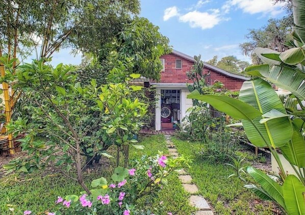 A house with a brick exterior, surrounded by lush greenery and a stone pathway leading to the entrance.