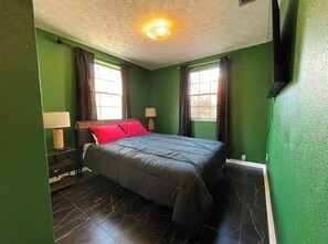 A bedroom with a bed, two bedside lamps, a window, and green walls.