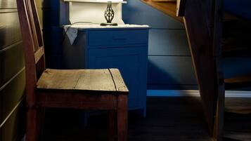 A rustic attic room with a wooden chair, a desk with a lamp, and a slanted ceiling.