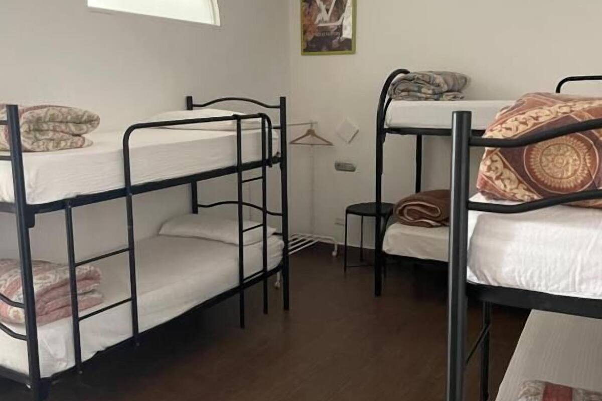 A dormitory room with bunk beds, a small table, and a window.