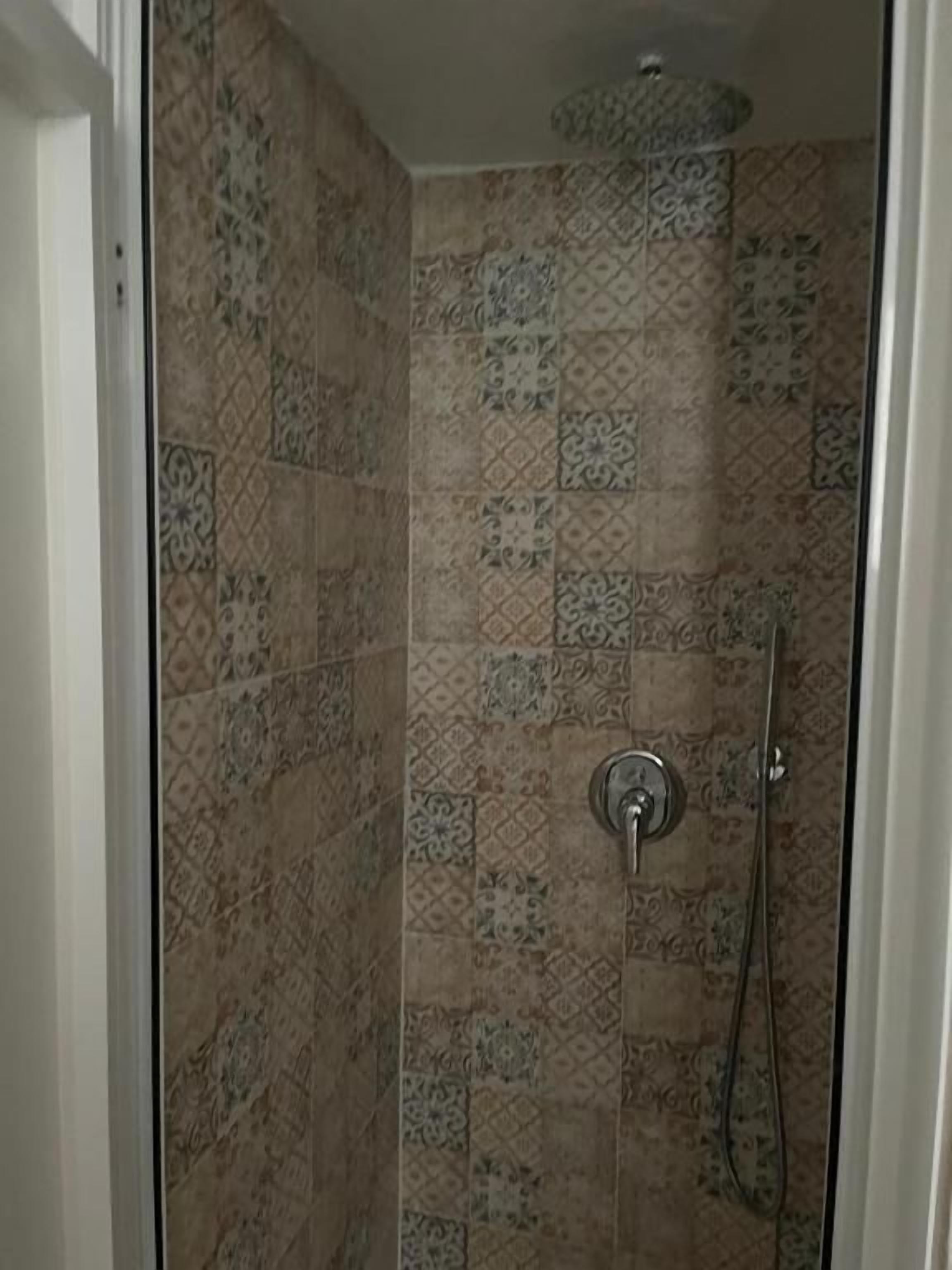 A shower with patterned tiles and a handheld showerhead.