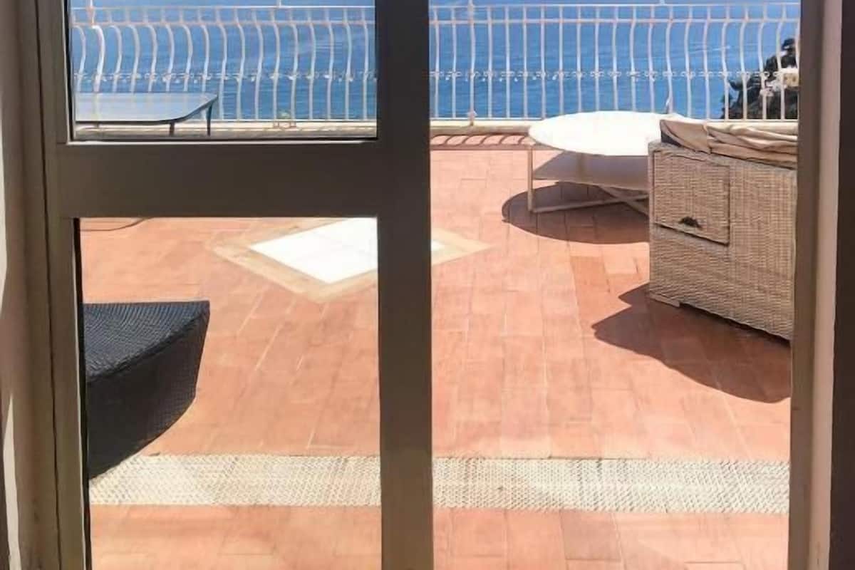 A balcony with a view of the sea, a white railing, and a wicker sofa.
