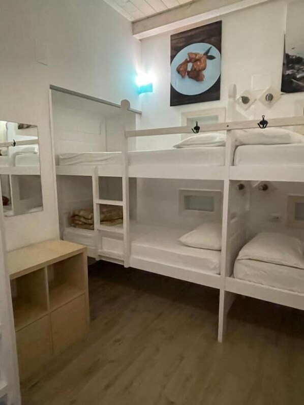 Une chambre avec un lit superposé, un plancher en bois, des murs blancs et une petite étagère.
