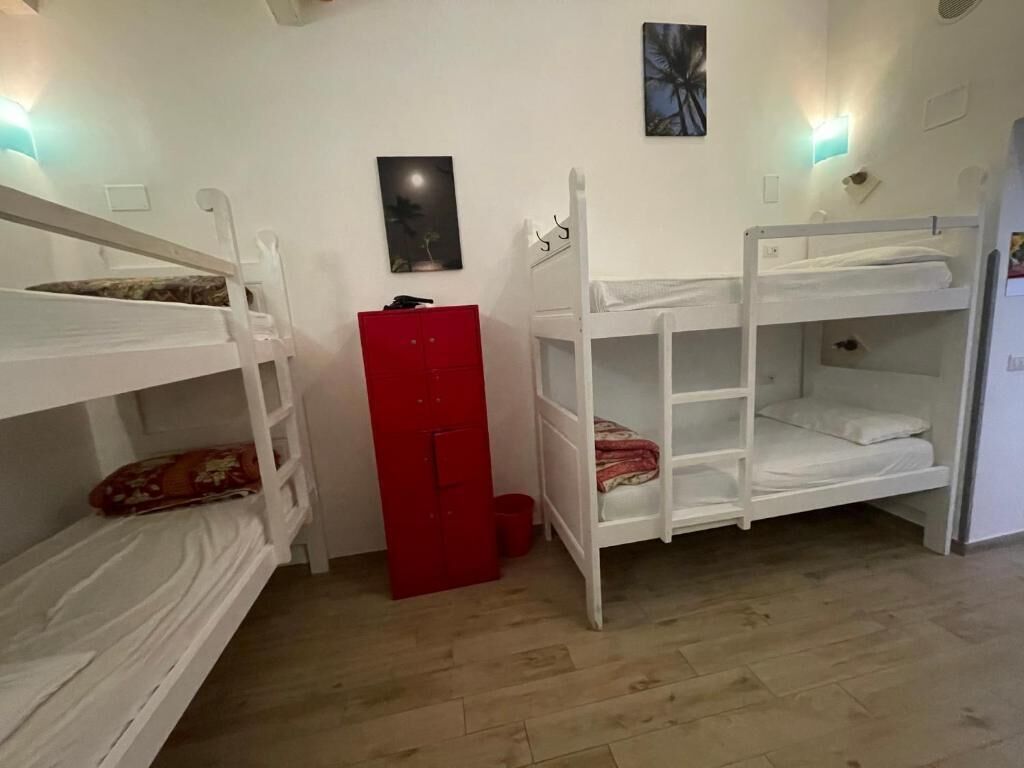 Une pièce avec des lits superposés, une armoire rouge et une petite poubelle.