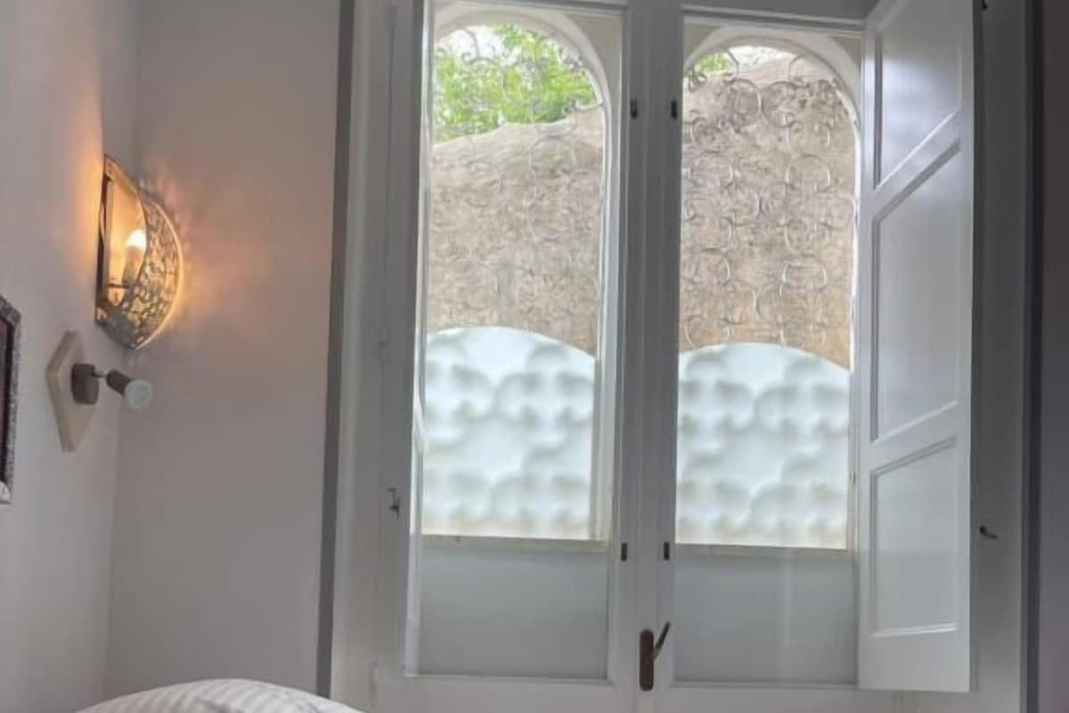 A bedroom with a bed, a window with frosted glass, and a wall-mounted light fixture.