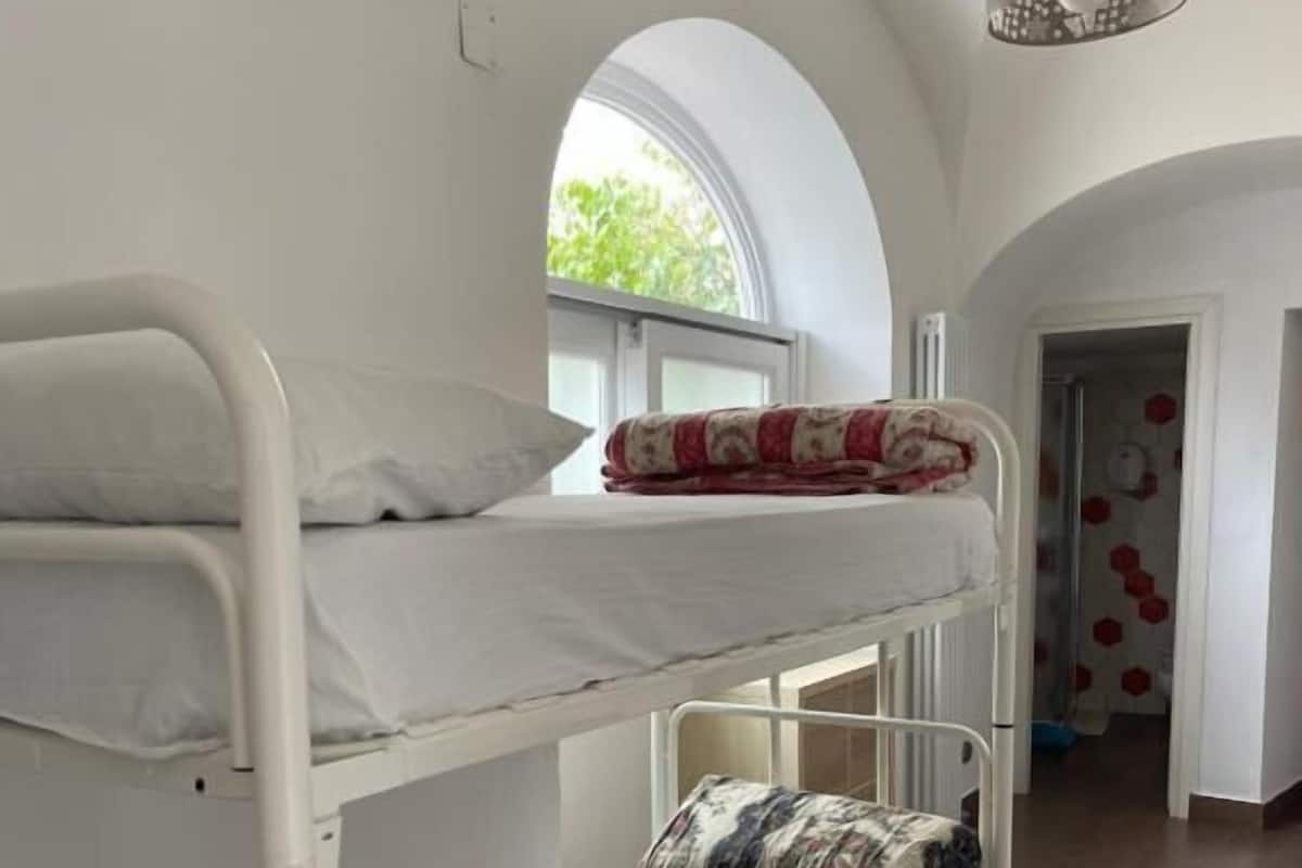 A bunk bed room with white bedding, a window with a view, and a hanging light fixture.