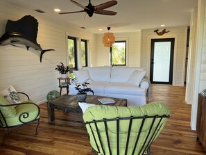 A living room with a white sofa, green chairs, a wooden coffee table, and a ceiling fan.