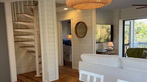 Un amplio salón con un sofá blanco, suelo de madera, una escalera y una gran lámpara de fibra trenzada.