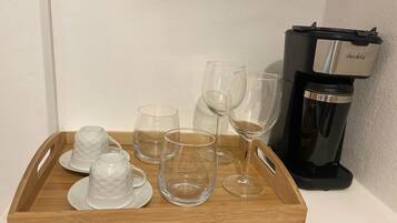 A wooden tray with clear glasses and a decakla coffee maker on a white surface.